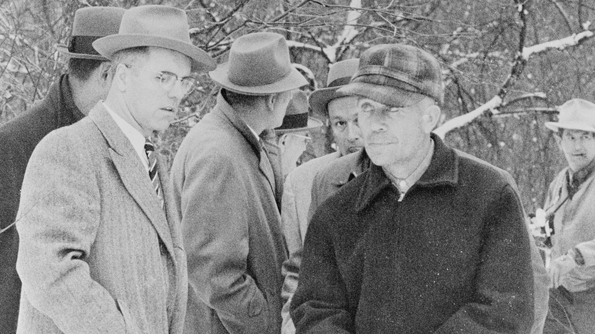 Ed Gein being surrounded by police in trench coats and fedoras