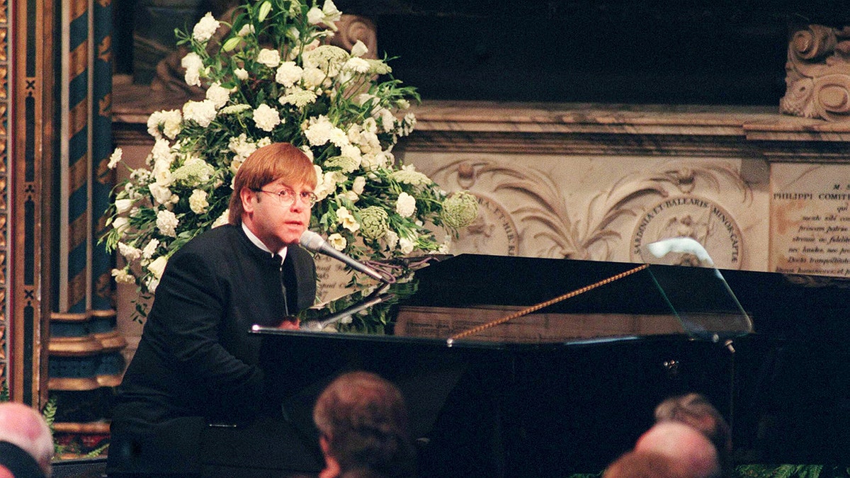 Elton John performing in front of a piano at a funeral
