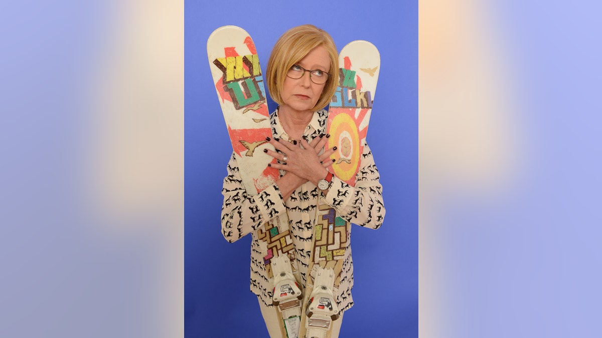 Eve Plumb holding skis in a multiprinted cardigan