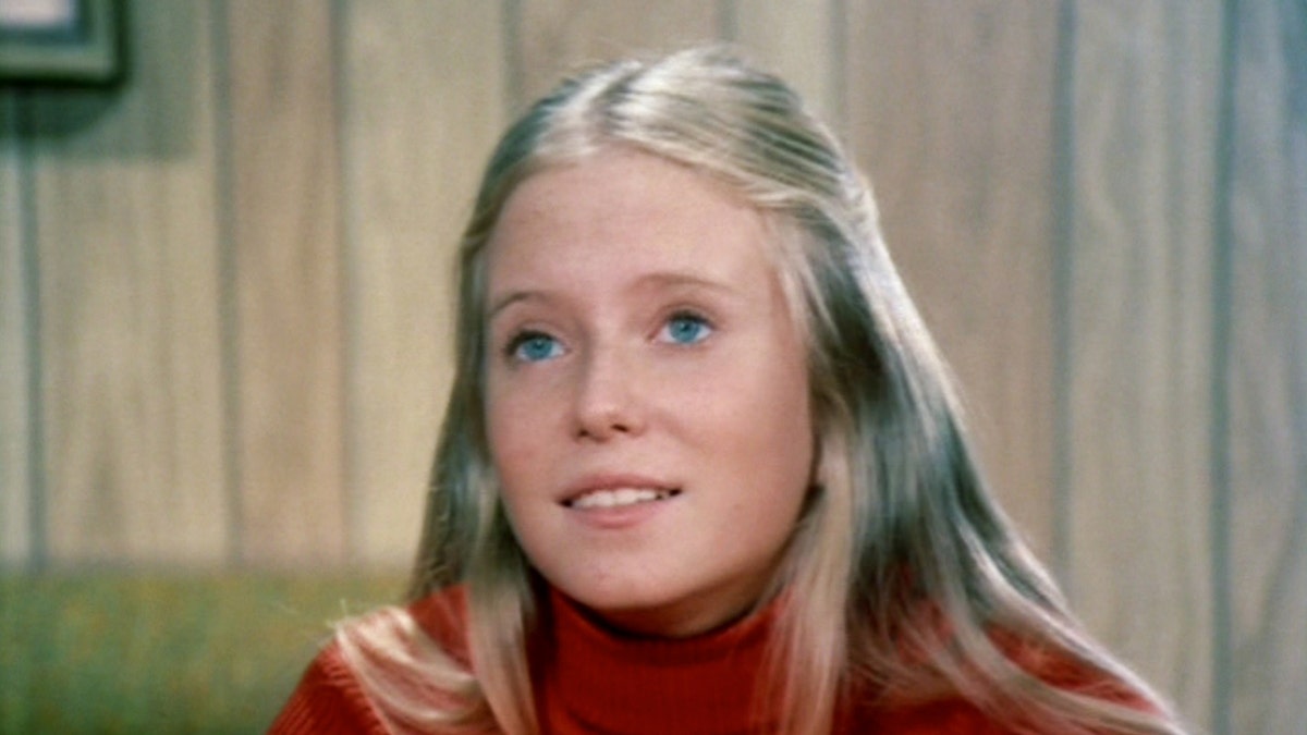 A close-up of Eve Plumb wearing a red sweater