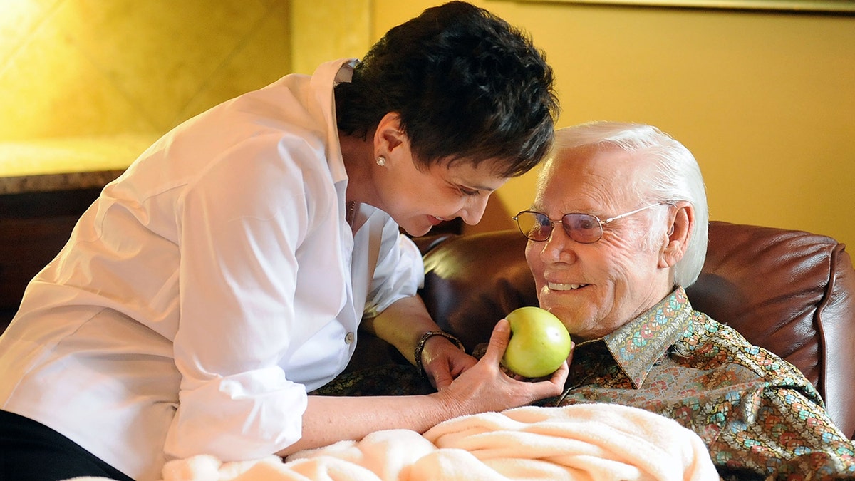 Nancy Jones wearing a white shirt giving George Jones a green apple