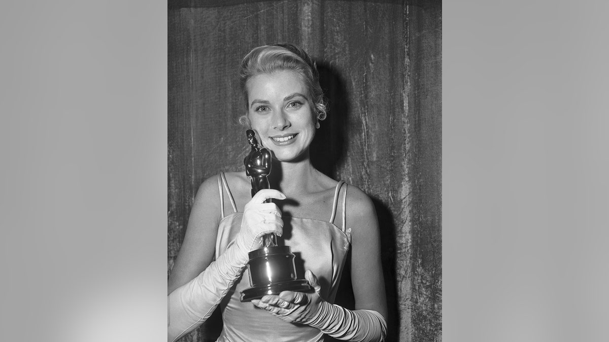Grace Kelly wearing a spaghetti strapped sain dress holding an Oscar