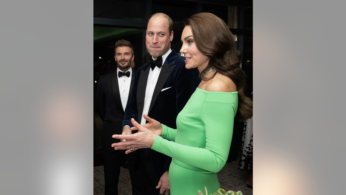 Kate Middleton wearing a lime green dress talking to someone as Prince William and David Beckham watch in tuxes