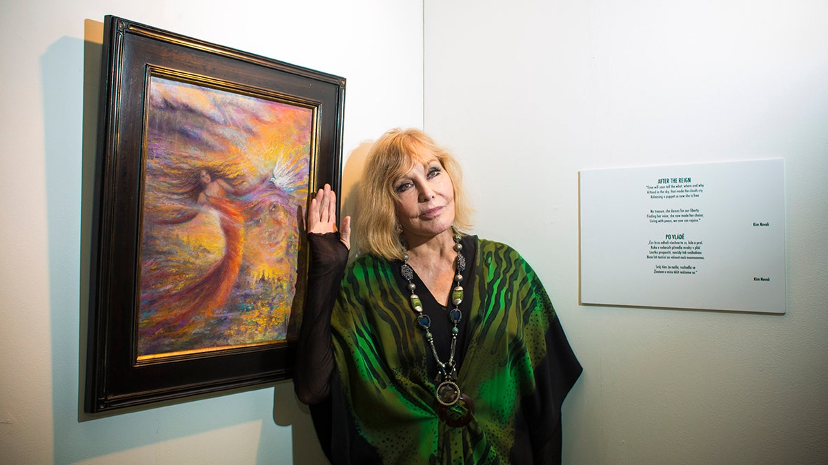 Kim Novak posing next to one of her paintings in a green gown