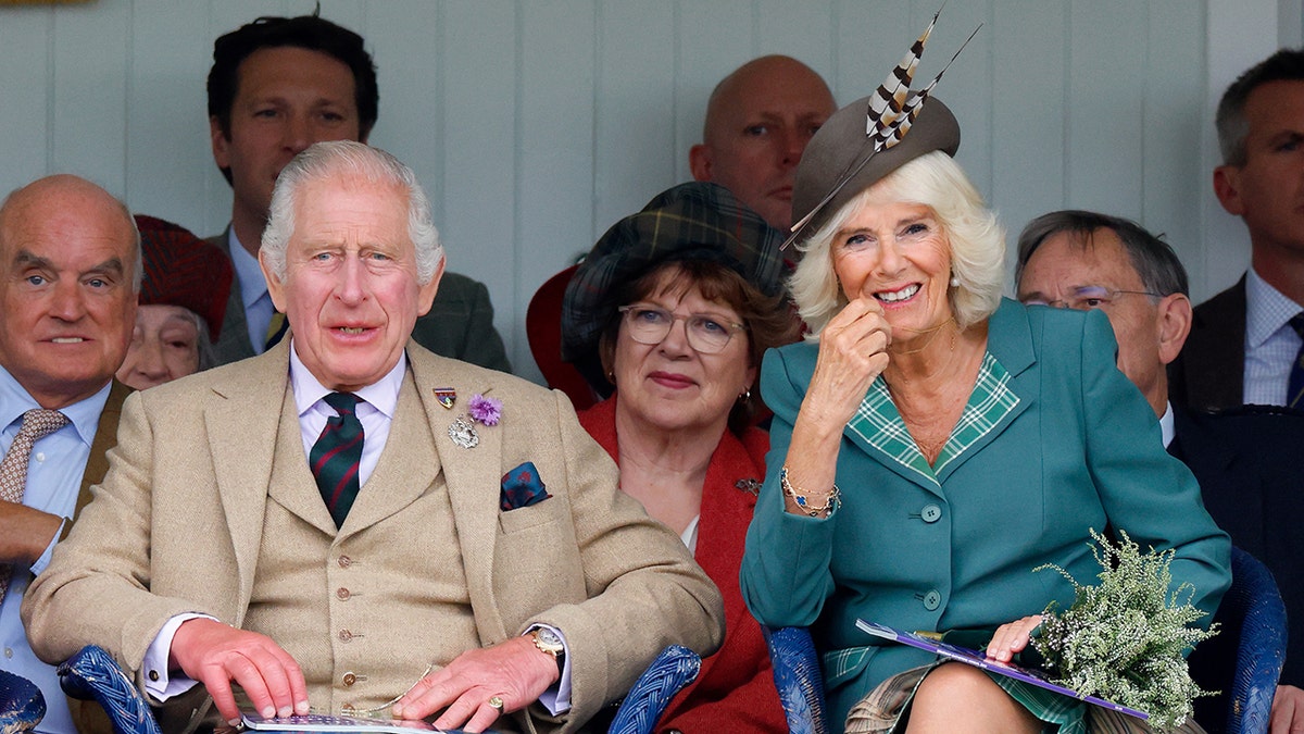A close-up of King Charles wearing a beige suit and Queen Camilla wearing a green dress and a matching hat