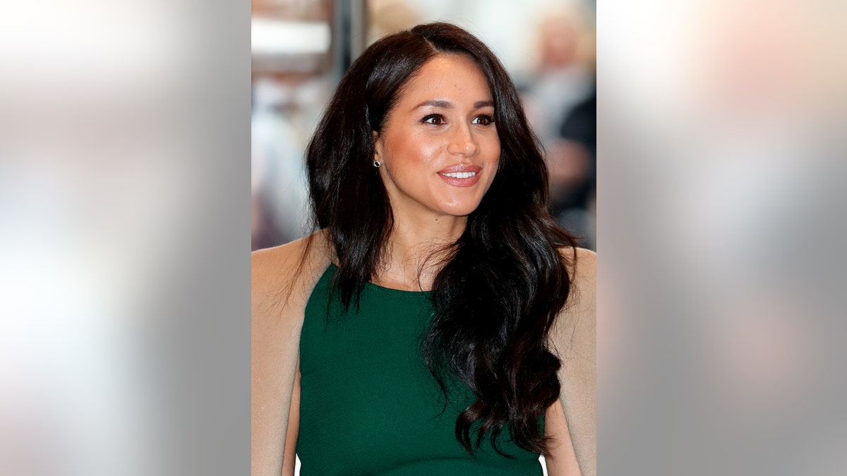 A close-up of Meghan Markle in a green dress and a camel hued coat