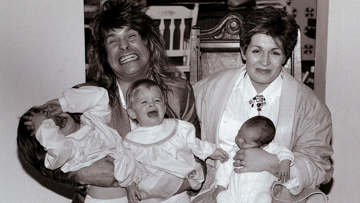A black-and-white photo of Sharon and Ozzy Osbourne holding their three young children