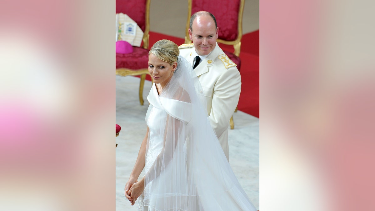 Princess Charlene wearing a white wedding dress next to Prince Albert in a white suit