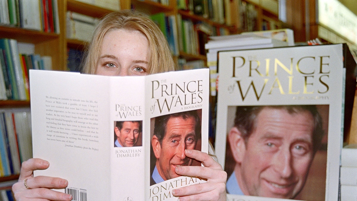 A woman holding up a book with Prince Charles on the cover