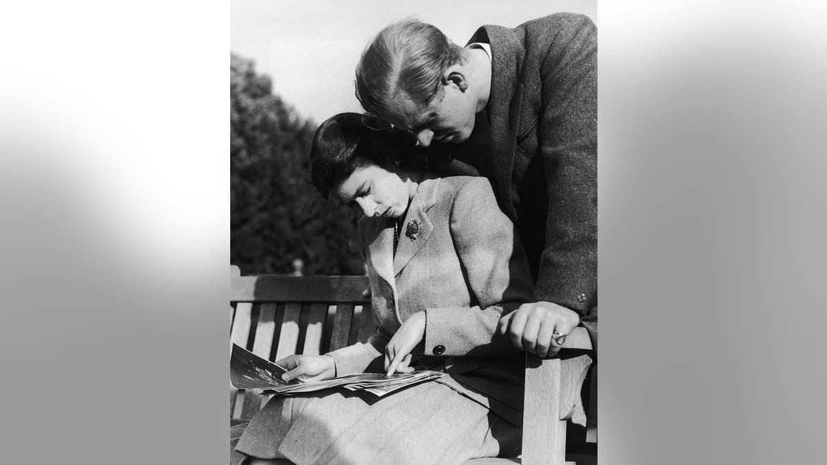 Prince Philip look down next to Queen Elizabeth as she looks at photographs