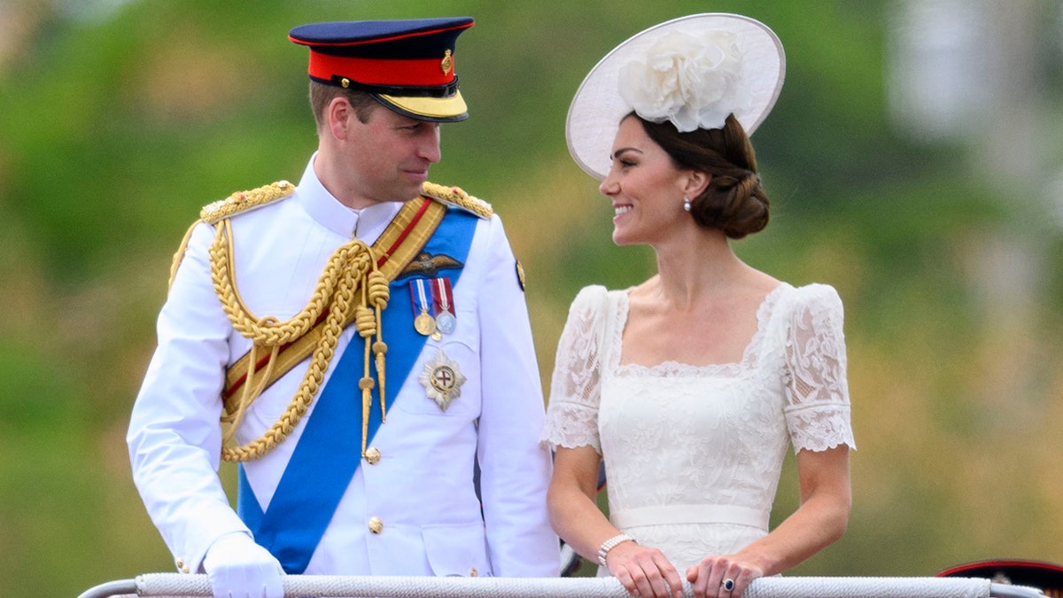 Príncipe William vestindo um terno militar branco ao lado de Kate Middleton em um vestido de renda branca e chapéu combinando