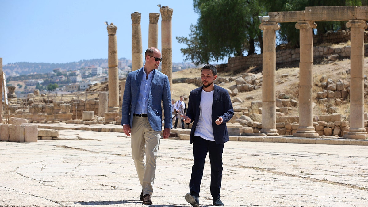 Prince William wearing a blue blazer, a blue shirt and beige pants walking alongside crown prince hussein also in casual wear