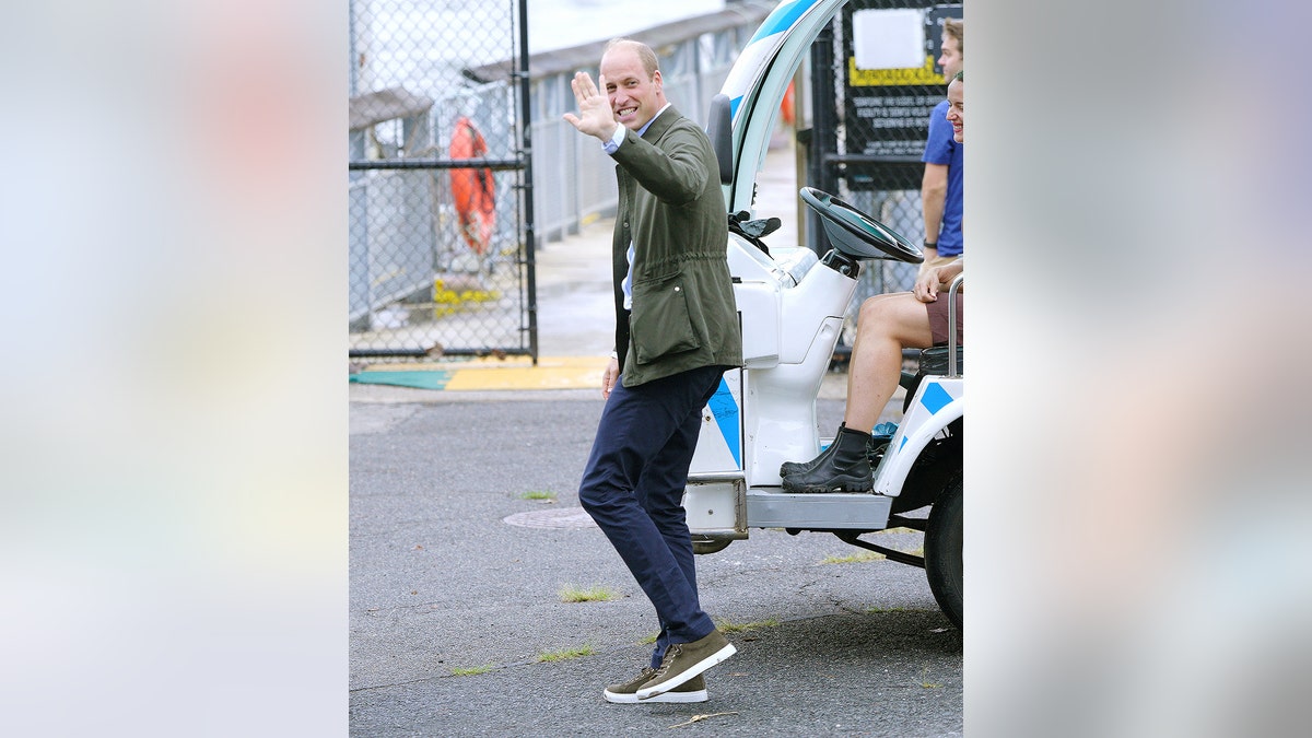 Prince William wearing blue pants, a hunter green jacket and matching sneakers