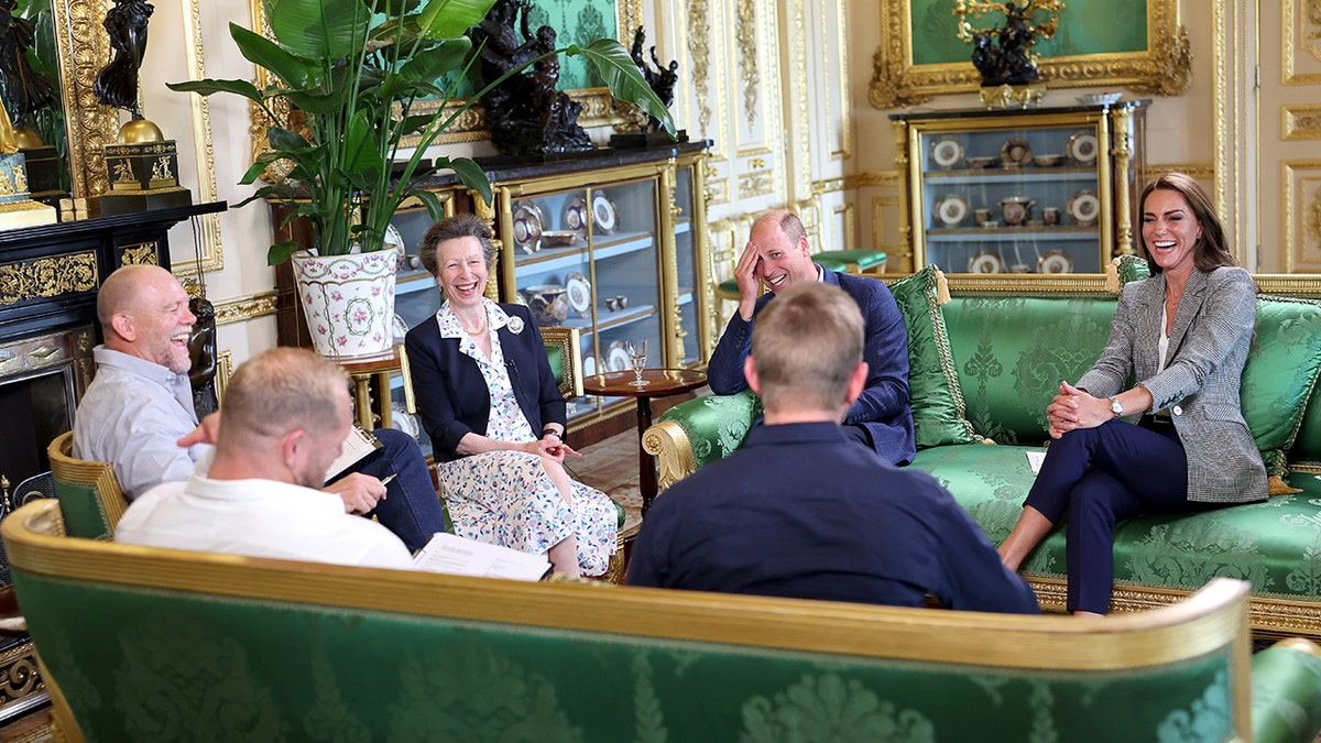 A group of British royals laughing together in a palace room recording a podcast