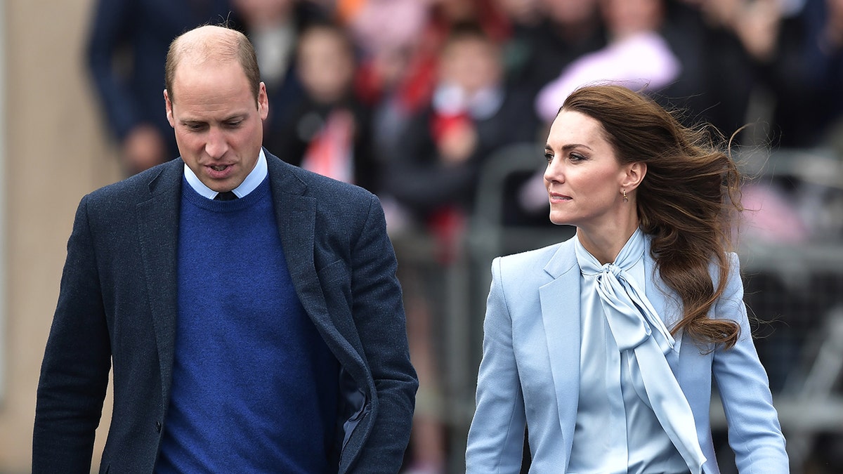 Prince William wearing a navy blazer and a blue sweater with Kate Middleton wearing a powder blue blouse