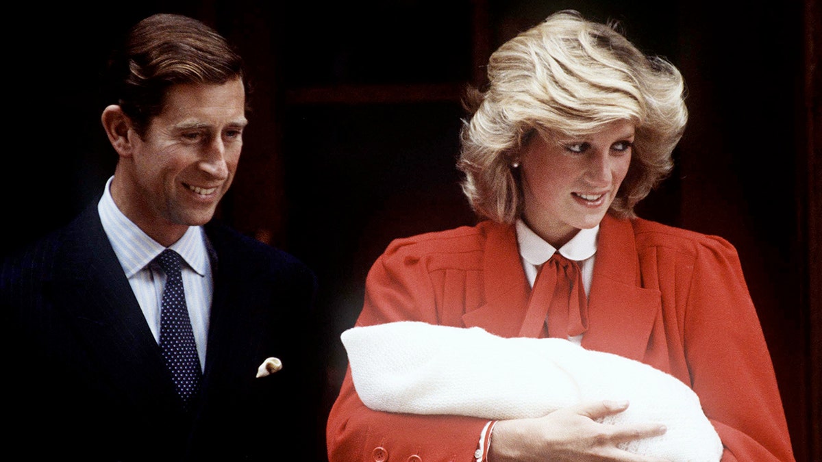 Princess Diana wearing a red dress holding baby Prince Harry next to Prince Charles in a dark suit