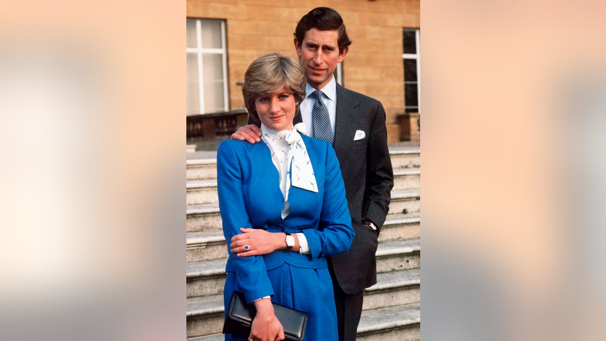 Princess Diana wearing a blue and white dress standing in front of Prince Charles in a grey suit