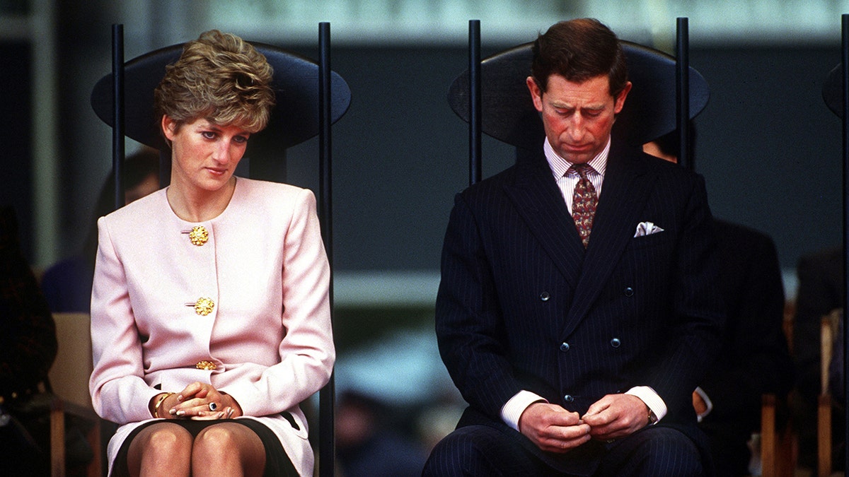 Princess Diana wearing a powder pink suit sitting next to Prince Charles in a dark suit