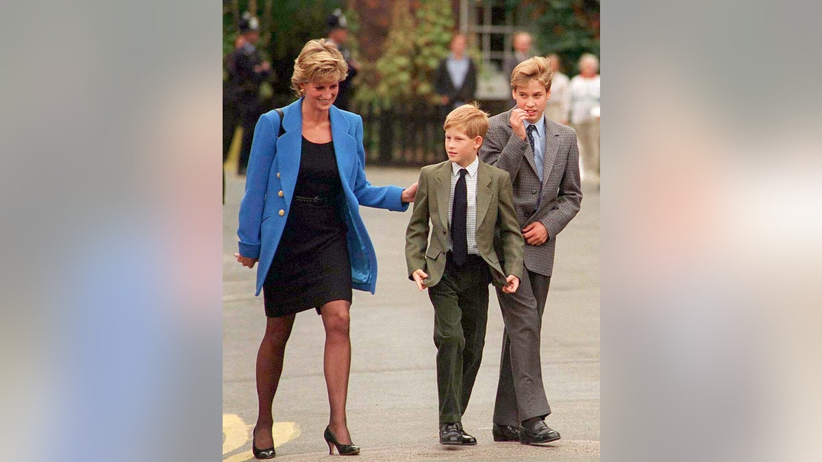 Princess Diana wearing a black dress and a blue blazer walking next to her two young sons