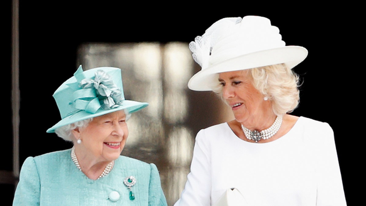 Queen Elizabeth wearing a light blue dress next to Camilla in a white dress and matching hat