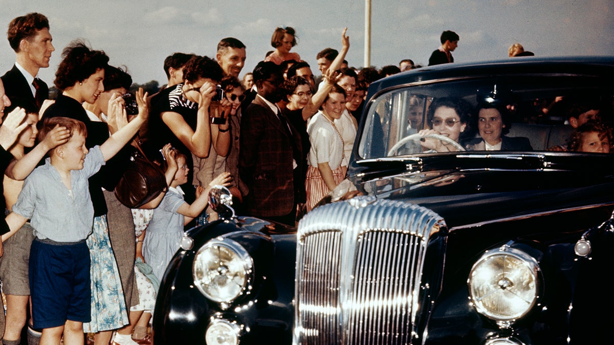 Queen Elizabeth driving next to a crowd