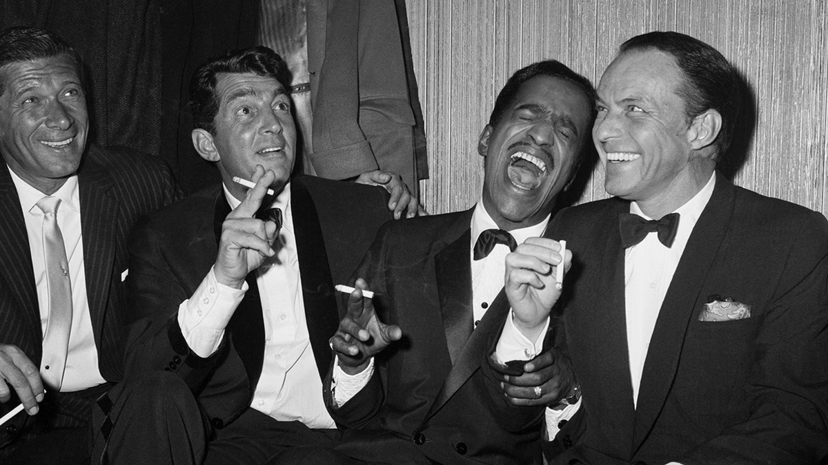 Sammy Davis Jr. laughing with members of the Rat Pack wearing matching tuxes