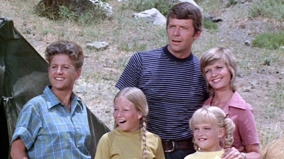 Cast mates of the Brady Bunch outdoors and smiling while looking away from the camera