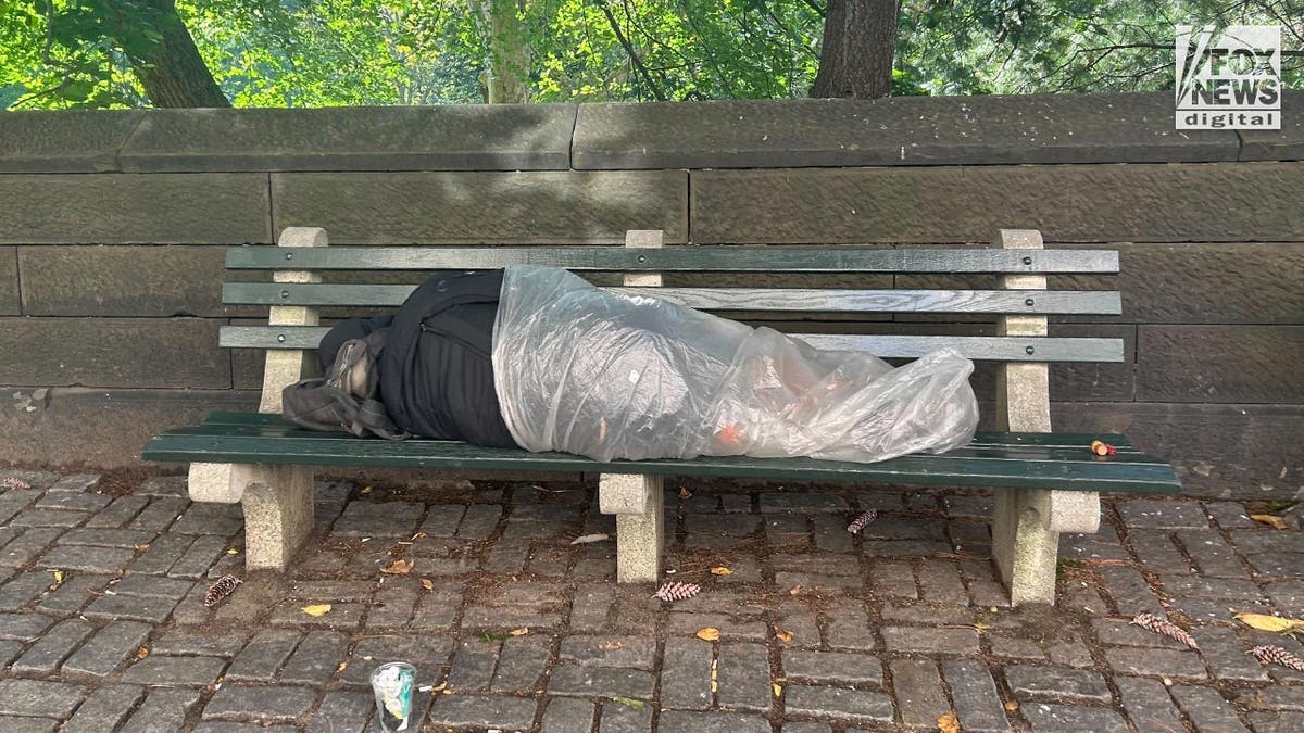 A person with their legs wrapped in a plastic bag lays on a bench