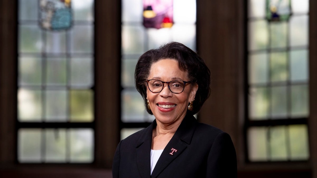 Acting Temple University President JoAnne Epps poses alone in front of stained glass windows and dark wooden walls