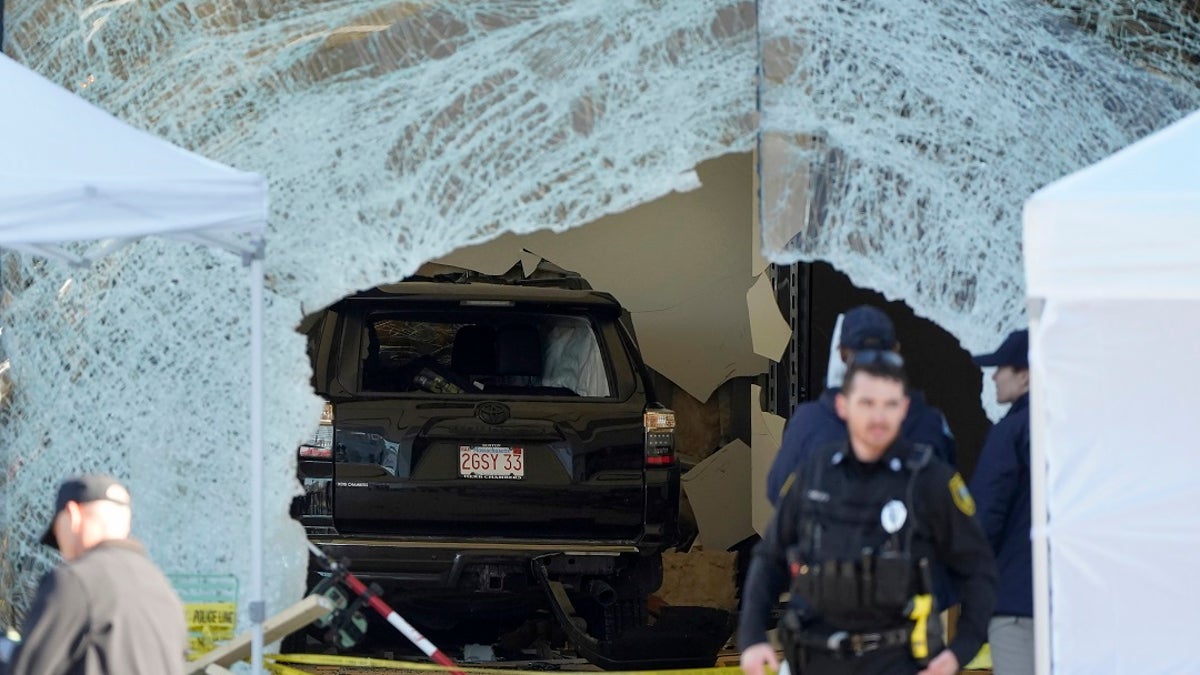  An SUV rests inside a Hingham, Massachusetts Apple store behind a large hole in the glass in front while the area is sealed off near police officers. 