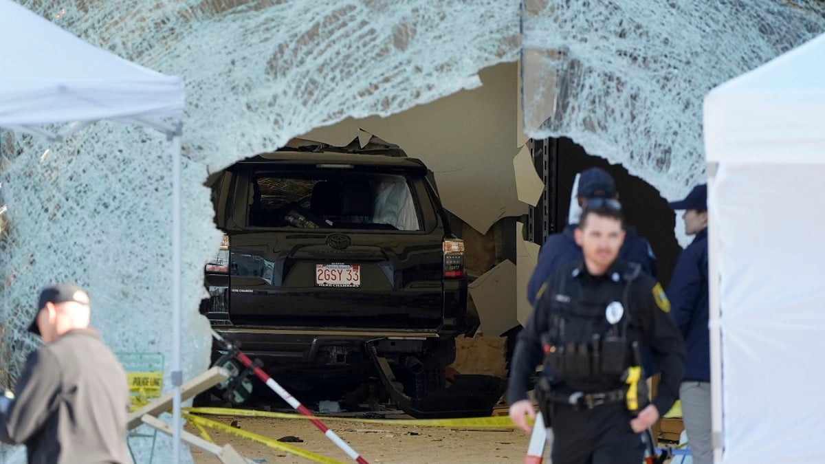 An SUV rests inside a Hingham, Massachusetts Apple store behind a large hole in the glass in front while the area is sealed off near police officers.
