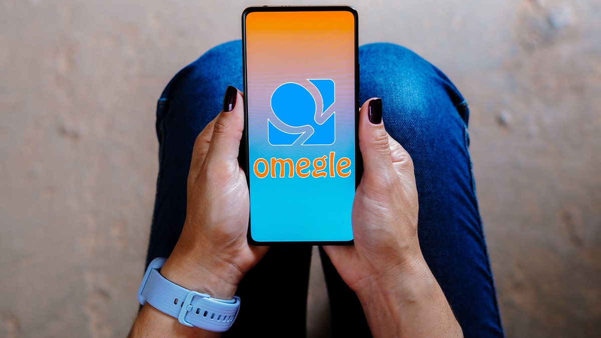Omegle app logo on phone screen held in seated woman's hands