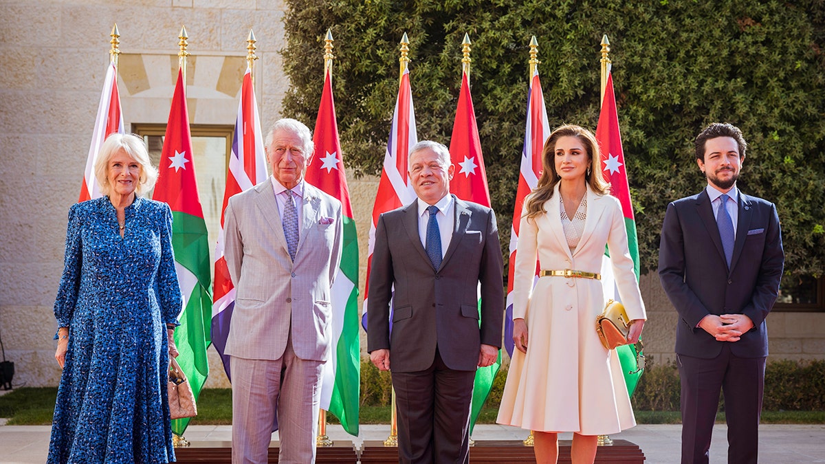 The royal family of Jordan in formal wearing standing next to Queen Camilla and King Charles in front of flags