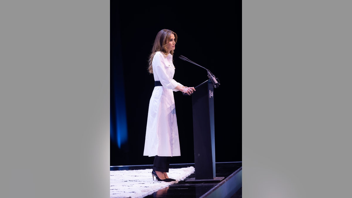 Queen Rania of Jordan wearing a white dress speaking in front of podium