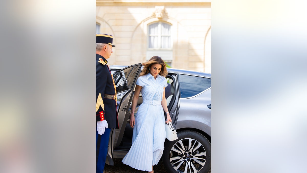 Queen Rania of Jordan wearing a white dress stepping out of a car