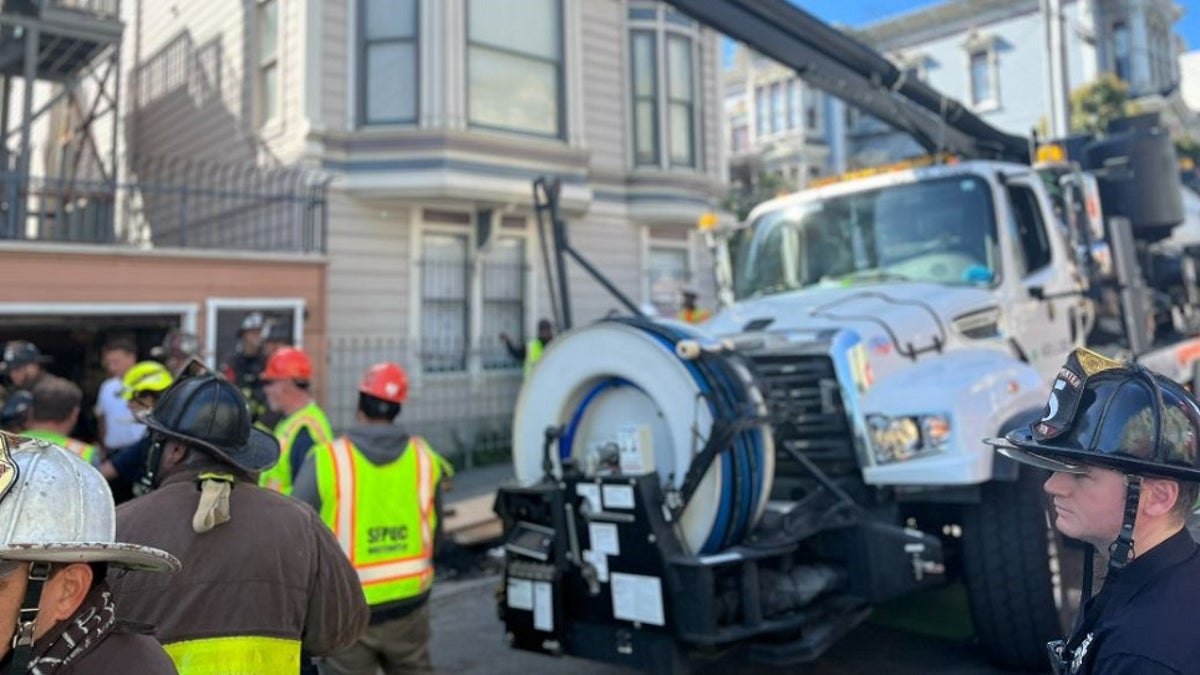 A large white vacuum truck is used to suck out dirt and debris from a hole on a San Francisco sidewalk
