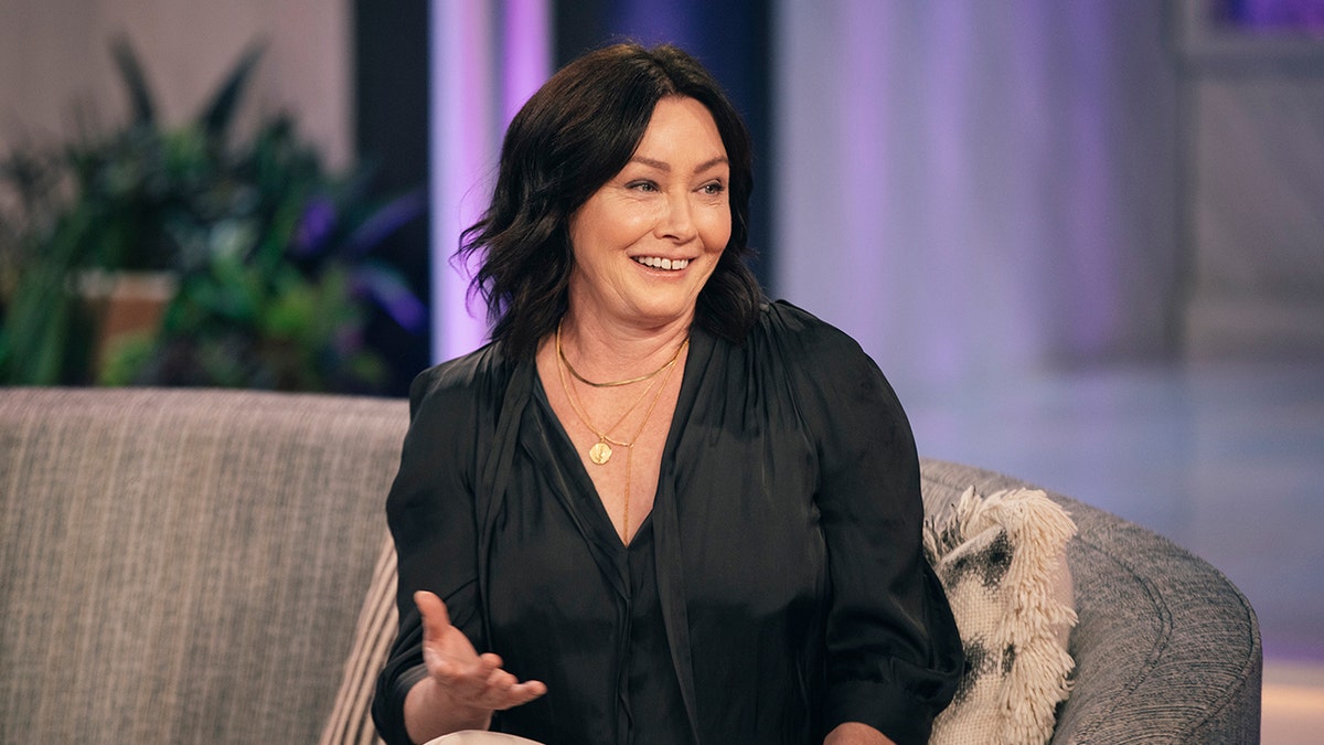 Shannen Doherty in a black blouse talks on TV