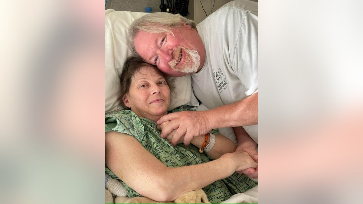 Dawn Lyn in a green hospital gown with her husband John Reese in a white shirt