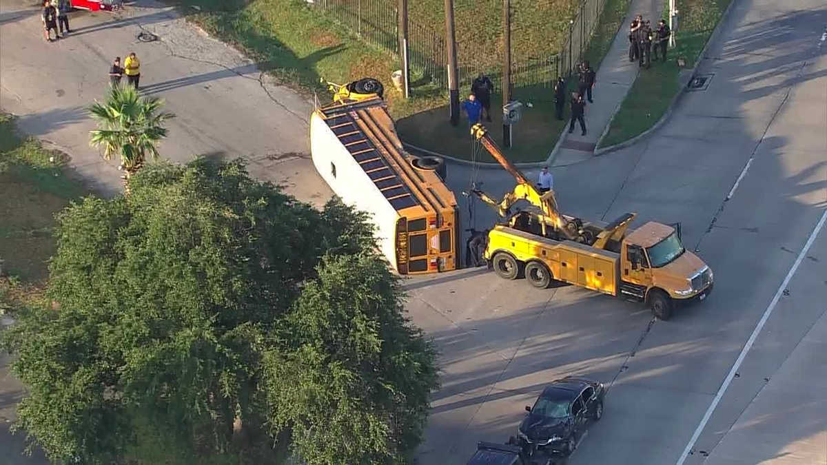 tow truck is seen by a Houston school bus on its side after a crash