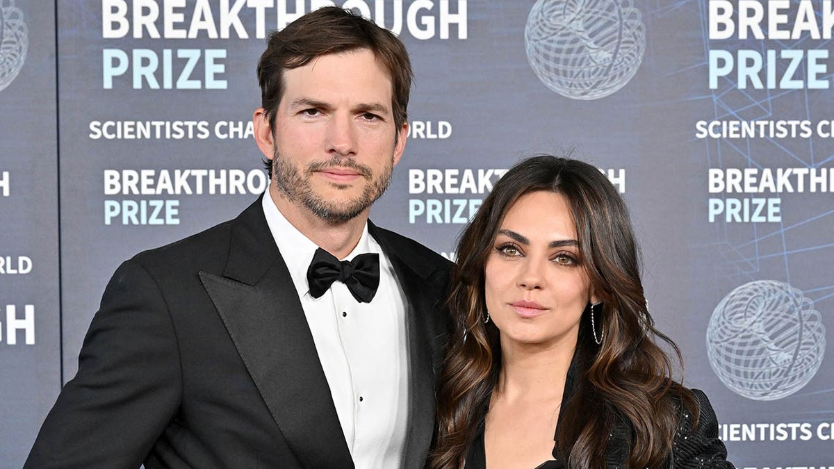 Ashton Kutcher in black tuxedo and Mila Kunis in a black dress on the carpet