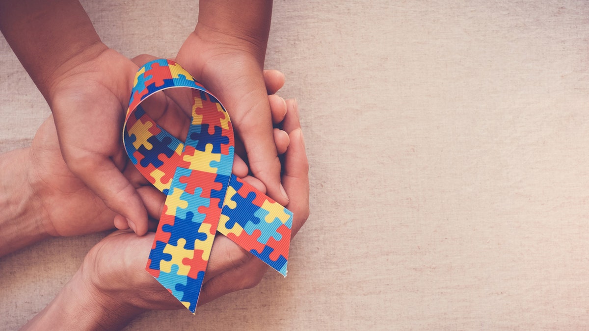 hands holding autism puzzle ribbon