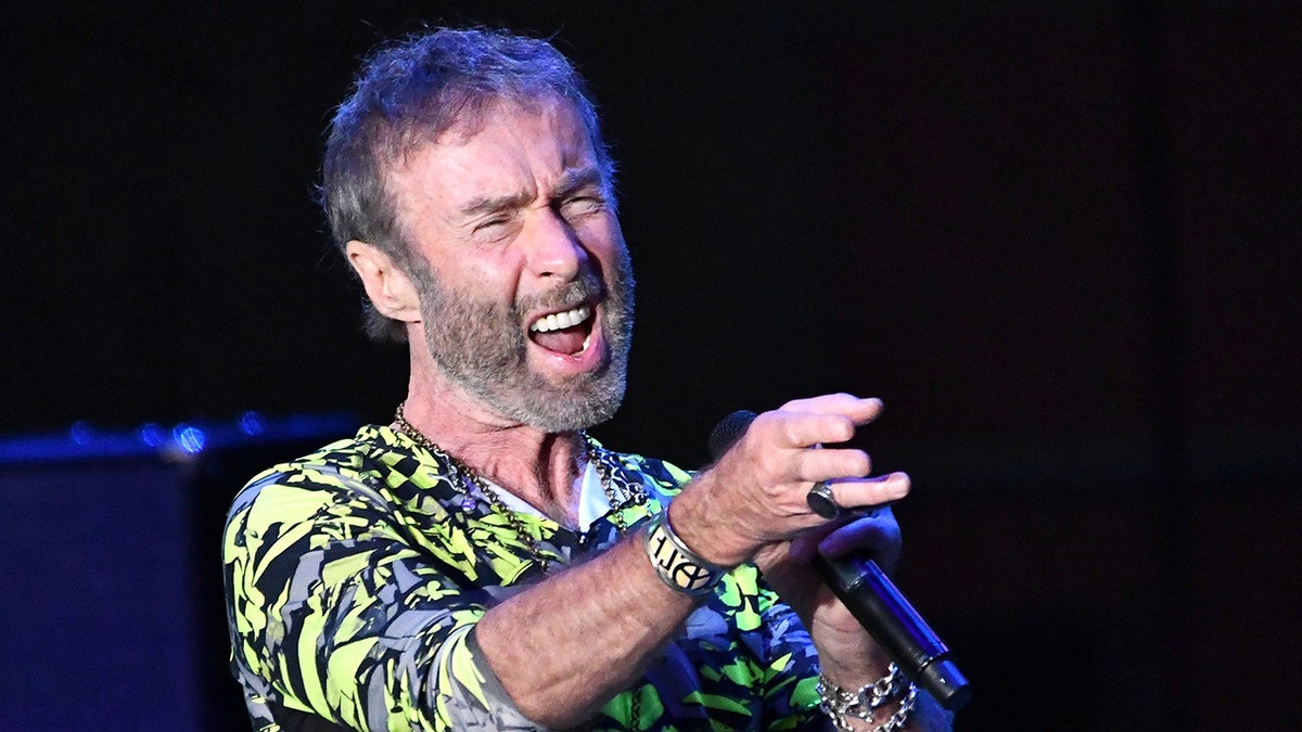 Paul Rodgers in a green printed shirt sings passionately on stage 