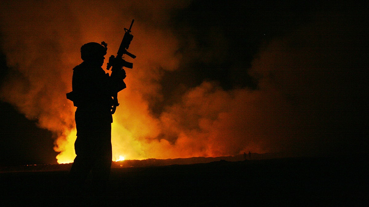 Silhouette of Marine standing in front of burn pit flames at night
