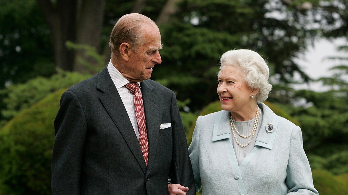 Prince Philip and Queen Elizabeth in formal wear smiling each other at a field