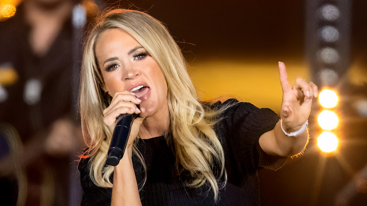 Carrie Underwood on stage in New York City sings into the microphone and points her finger out