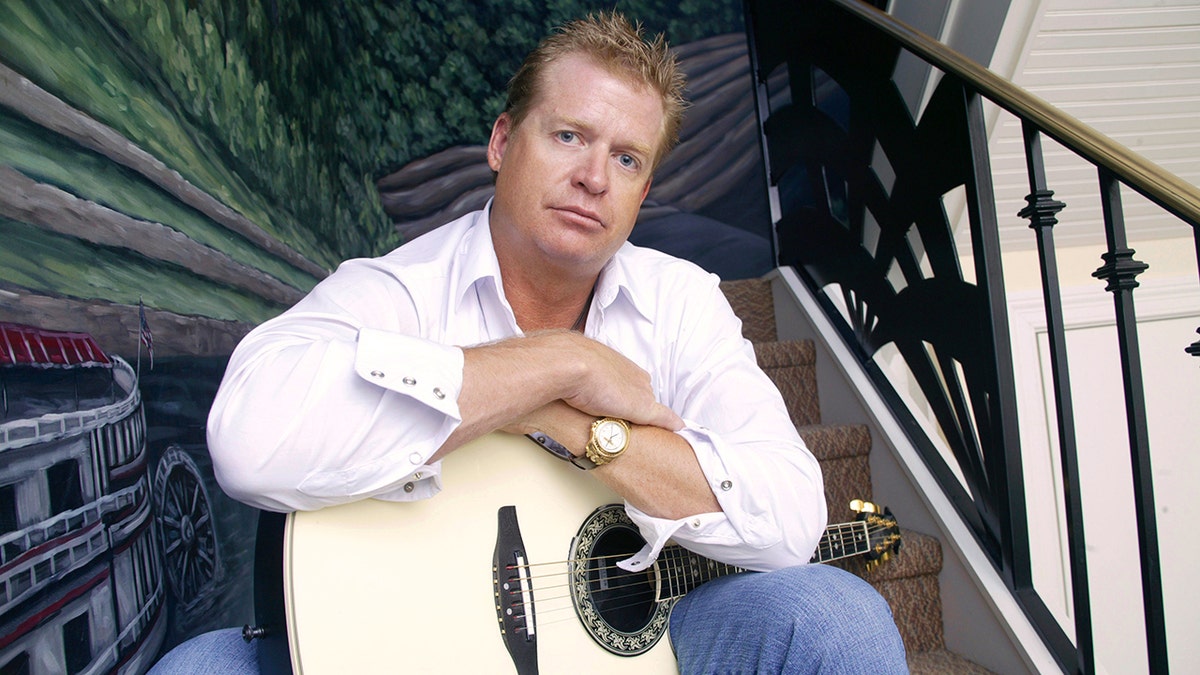 Charlie Robison holds a white guitar while sitting on a staircase