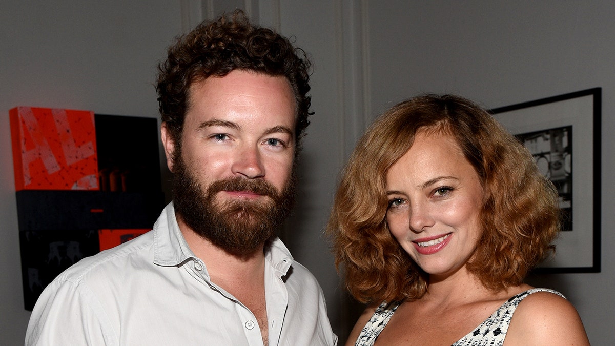 Danny Masterson in a white shirt smiles next to wife Bijou Phillips in a white and blue patterned top