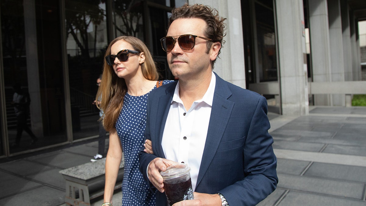 Bijou Phillips in a blue polka dot dress holds on to Danny Masterson's arm in a navy suit as they leave court