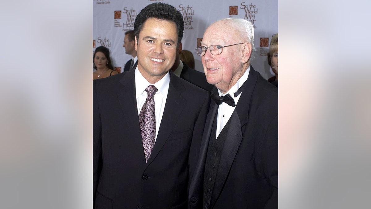 Donny Osmond in a black suit and light purple tie smiles with his father in a Tuxedo at a gala in Minnesotta