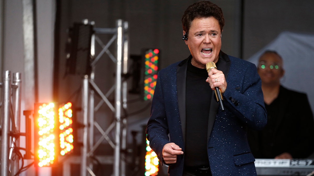 Donny Osmond sings passionately into the microphone in a glittery blue suit in New York